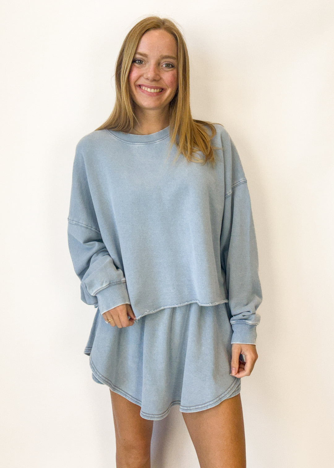 Woman wearing a light blue oversized sweatshirt against a plain background