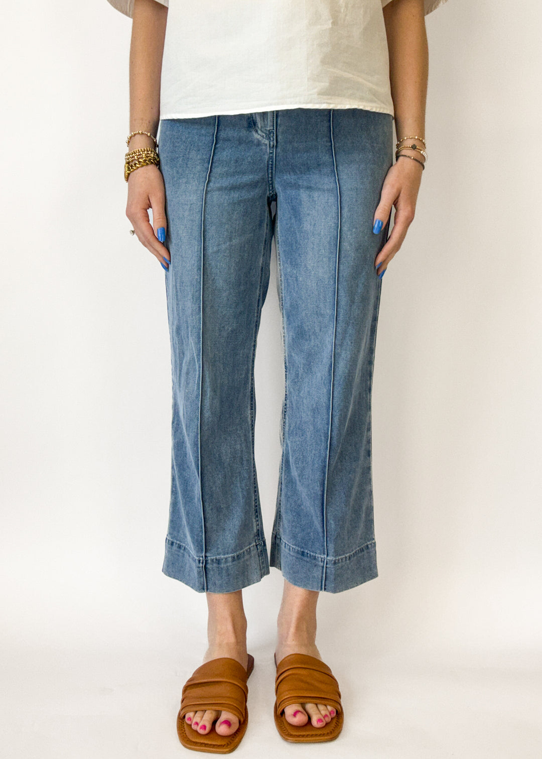 Person wearing blue jeans and brown sandals on a white background