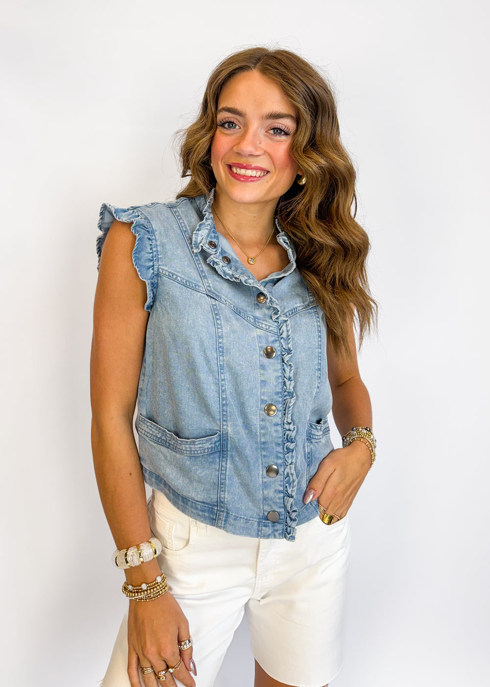 Woman wearing a denim vest over a white top on a plain background