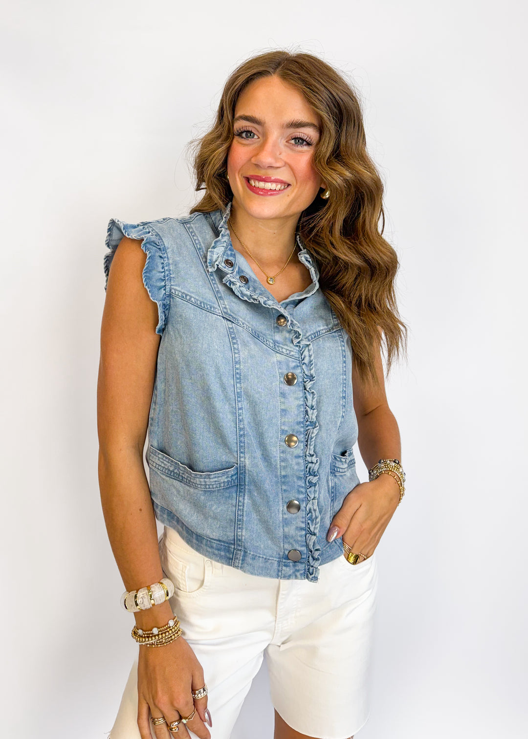 Woman wearing a denim vest over a white top on a plain background