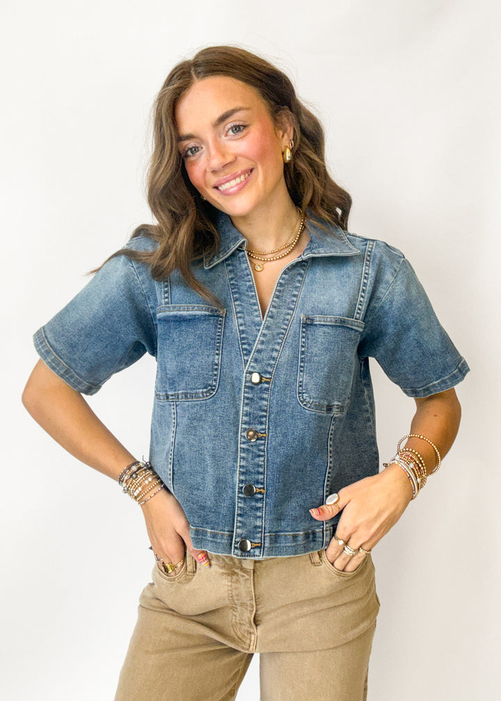 A woman modeling a short-sleeve blue denim button-up shirt with chest pockets, 