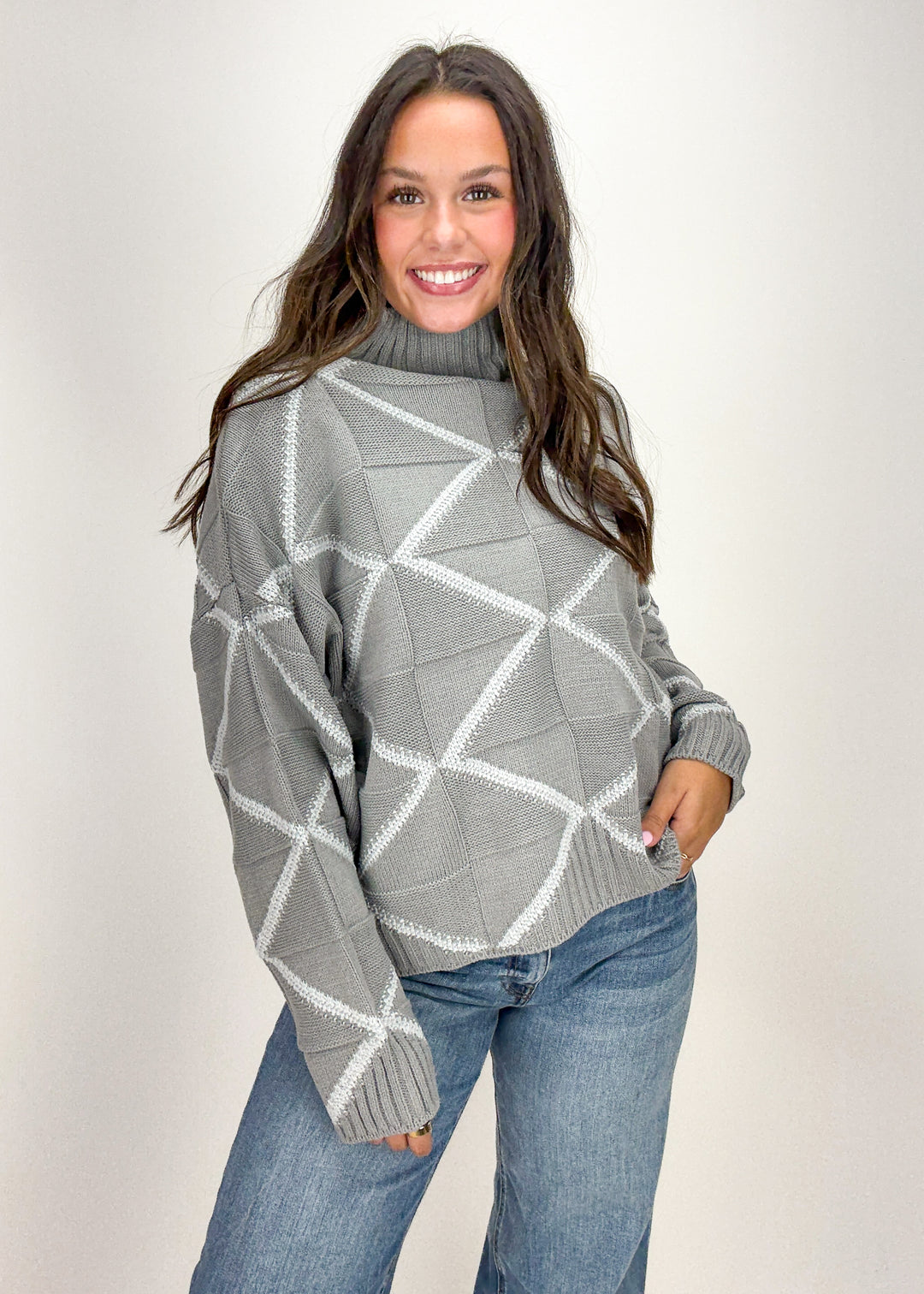Woman wearing a gray geometric patterned sweater and blue jeans 