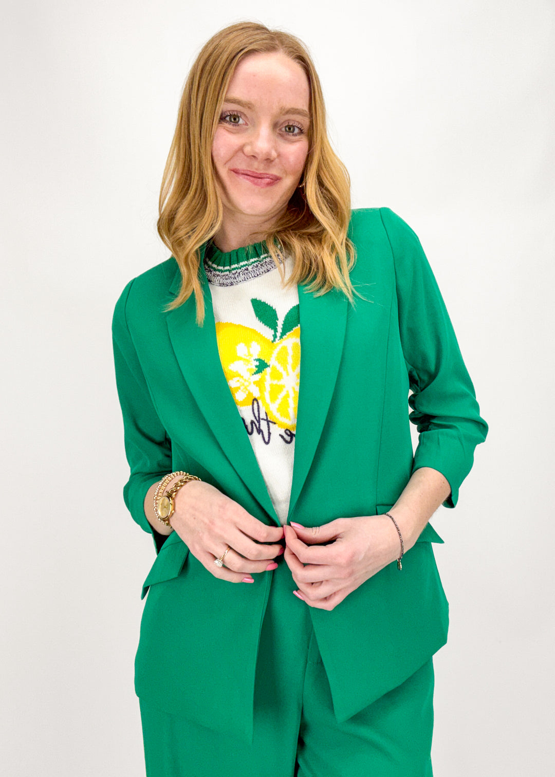 Woman wearing a green suit with a white shirt featuring a lemon design on a plain background