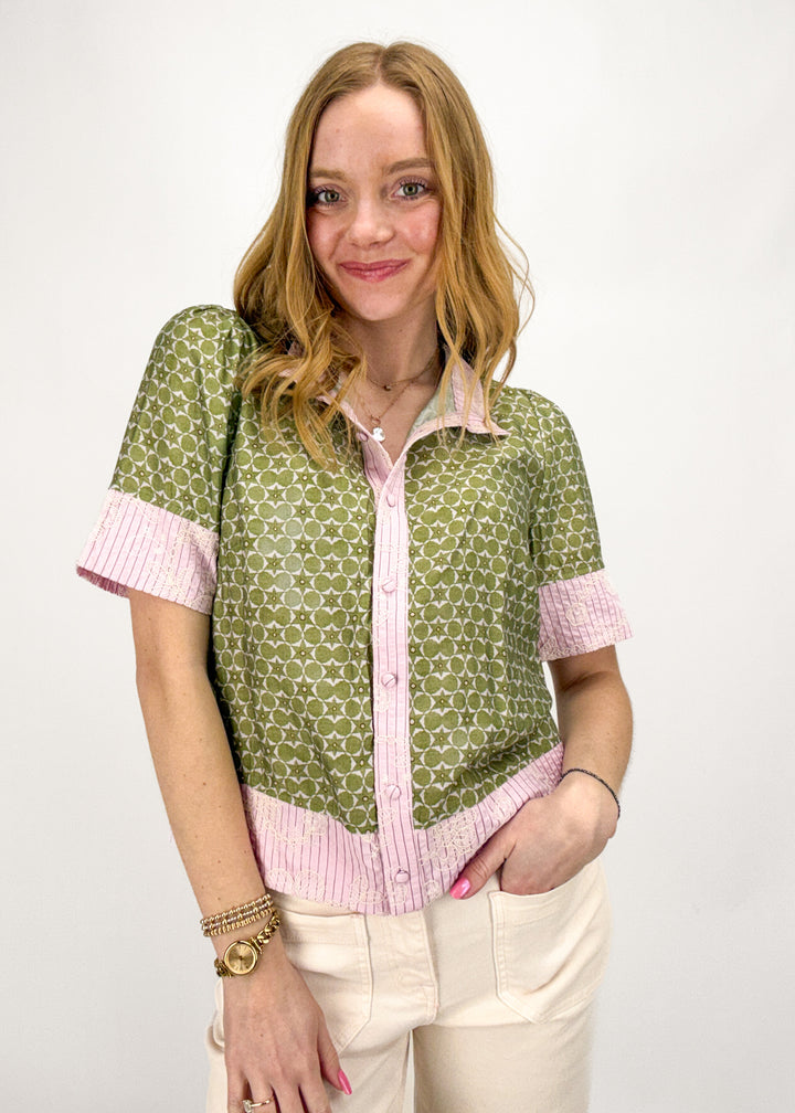 Woman wearing a green patterned shirt with pink trim on a white background