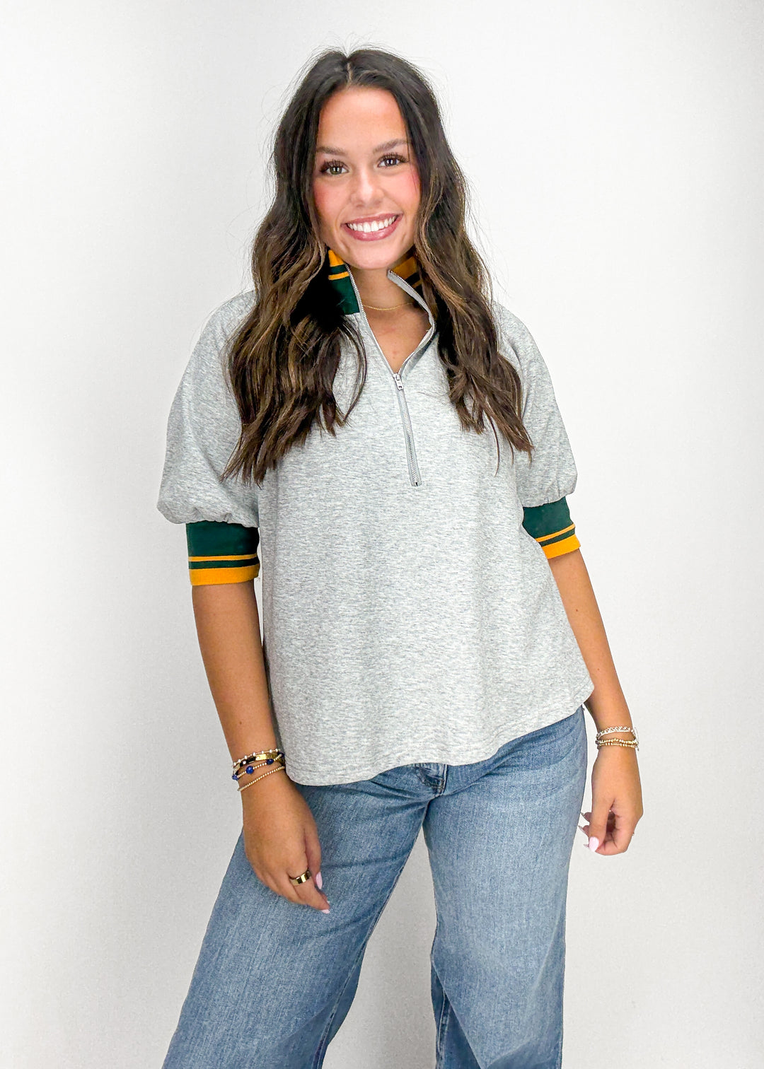 Woman wearing a gray polo shirt with green and yellow accents and blue jeans 