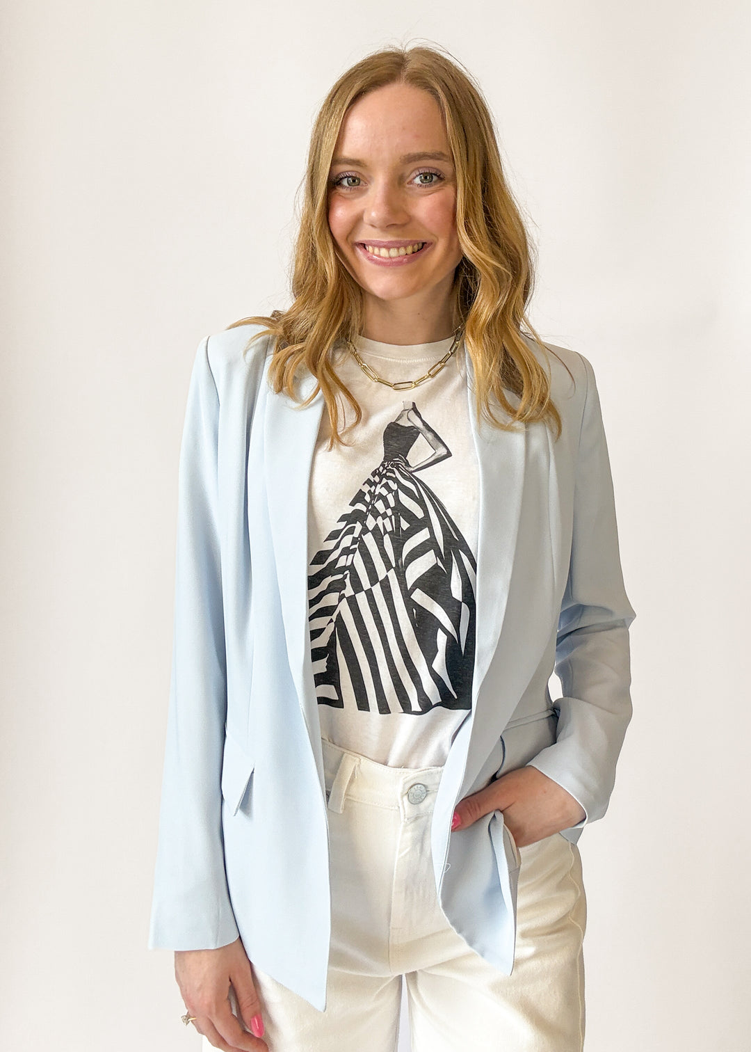 Woman wearing a light blue blazer over a graphic t-shirt with a white background