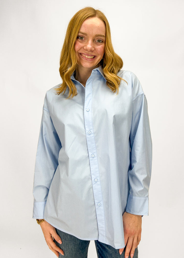 Woman wearing a light blue button-up shirt against a white background
