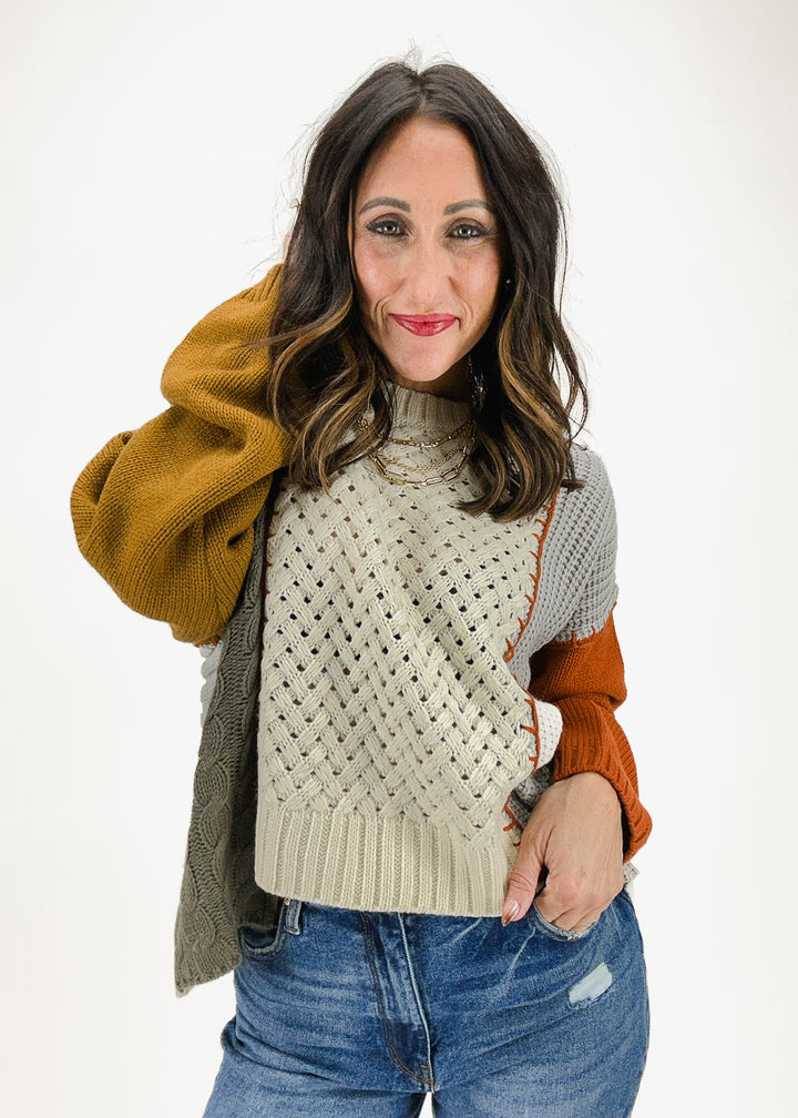 A women's multicolor knit sweater featuring a textured pattern with color block sections in mustard, beige, gray, and burnt orange, creating a cozy and stylish look.