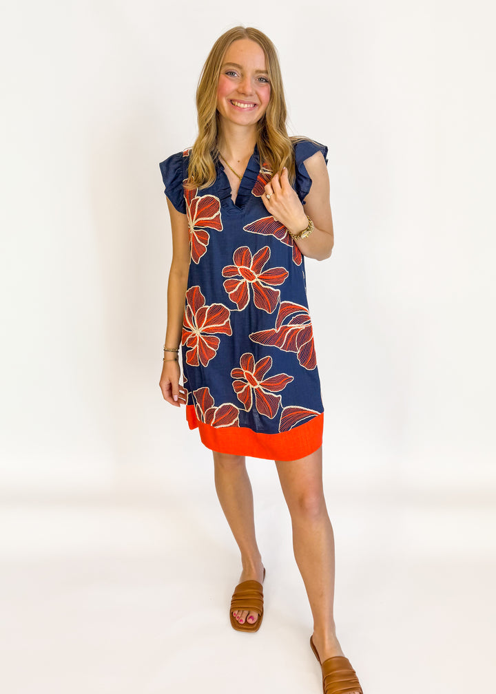 Woman wearing a navy dress with red floral pattern on a white background