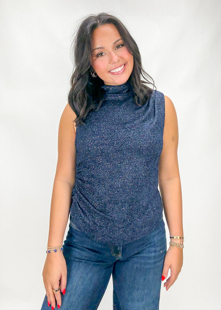 Woman wearing a blue sleeveless top and jeans against a white background
