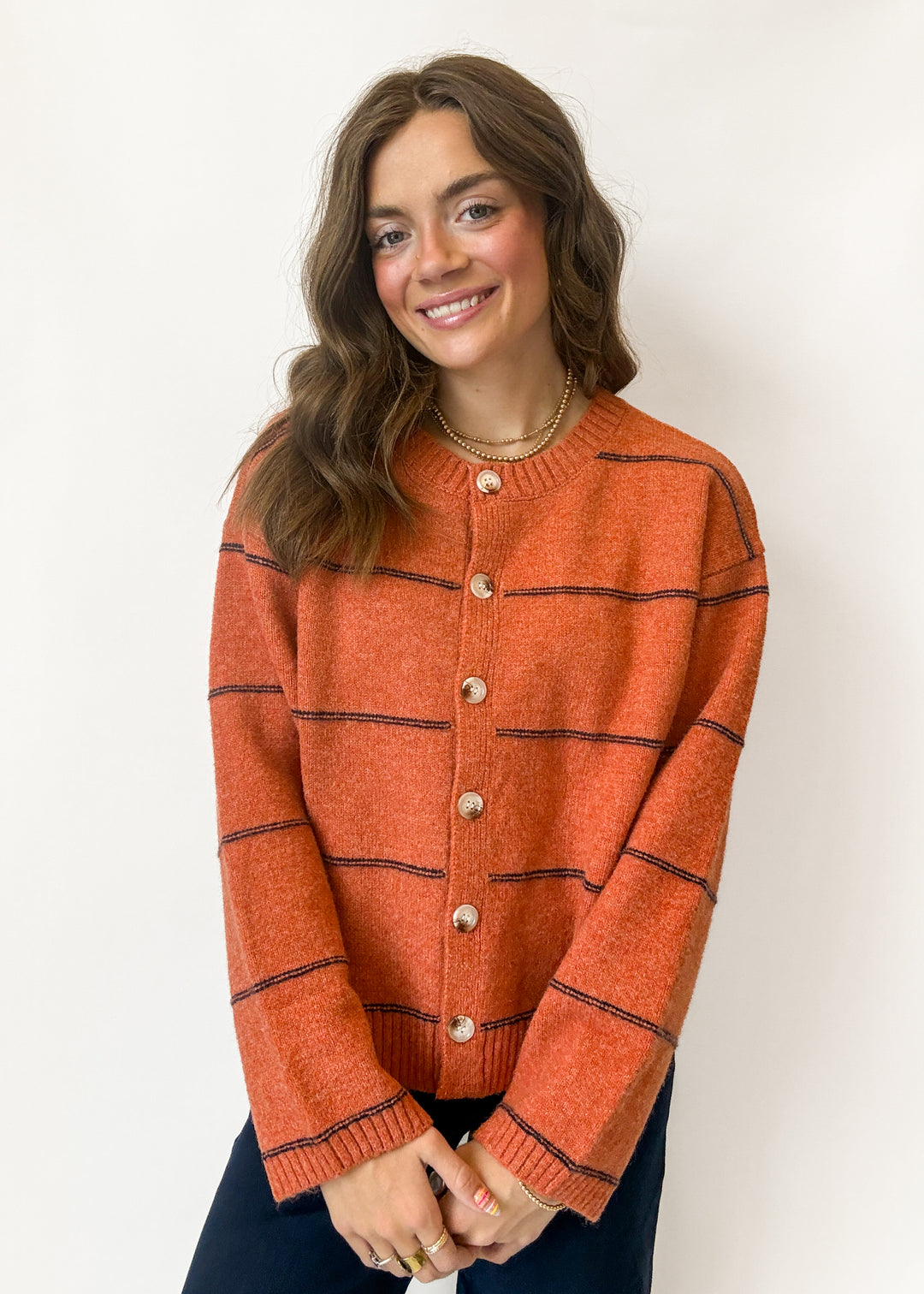 A woman wearing a rust-orange knit cardigan with thin black horizontal stripes and gold-tone buttons