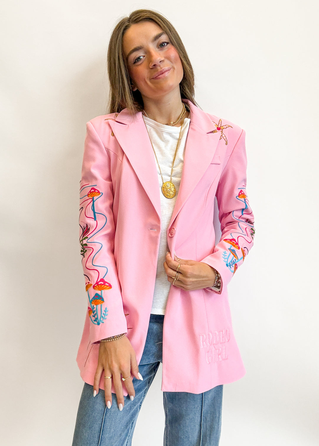 Person wearing a pink blazer with colorful embroidery on sleeves against a white background