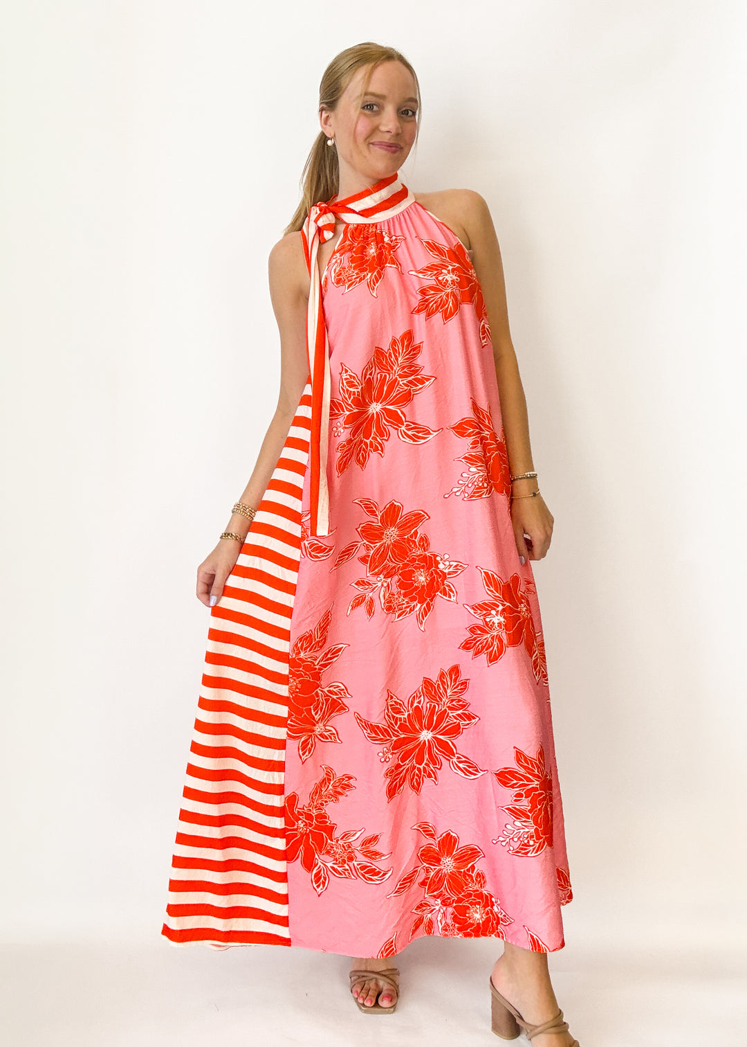 Woman wearing a pink dress with red floral patterns and a striped red and white sleeve.