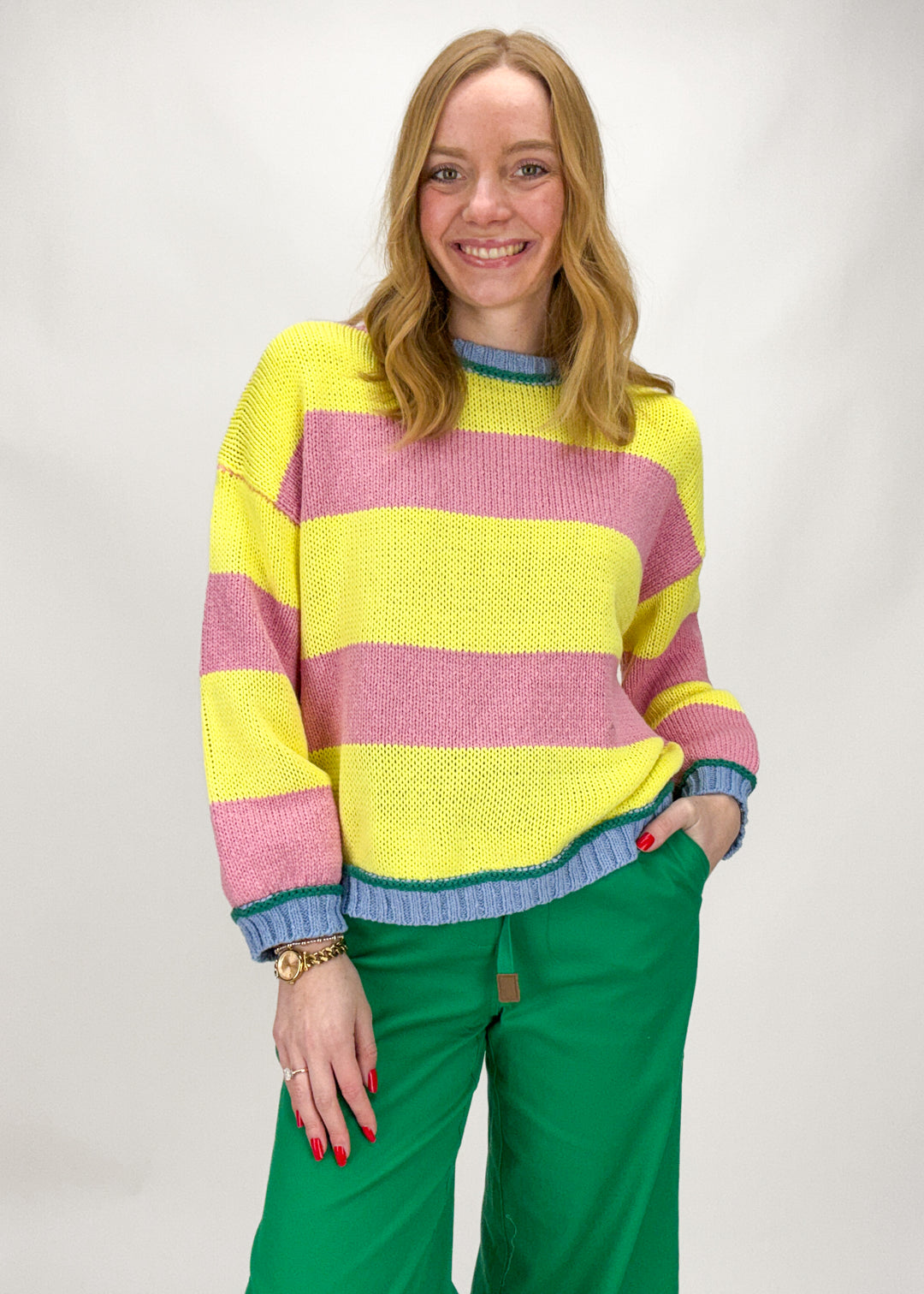 Person wearing a colorful striped sweater and green pants on a white background