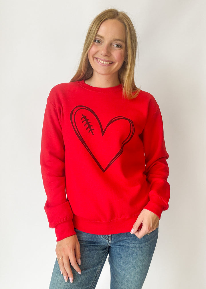 Person wearing a red sweatshirt with a black heart design on a plain background