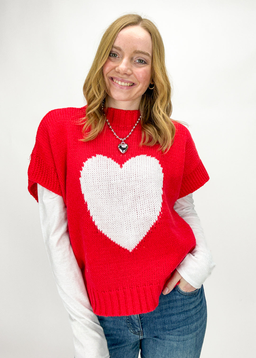 Person wearing a red sweater with a white heart design on a plain background