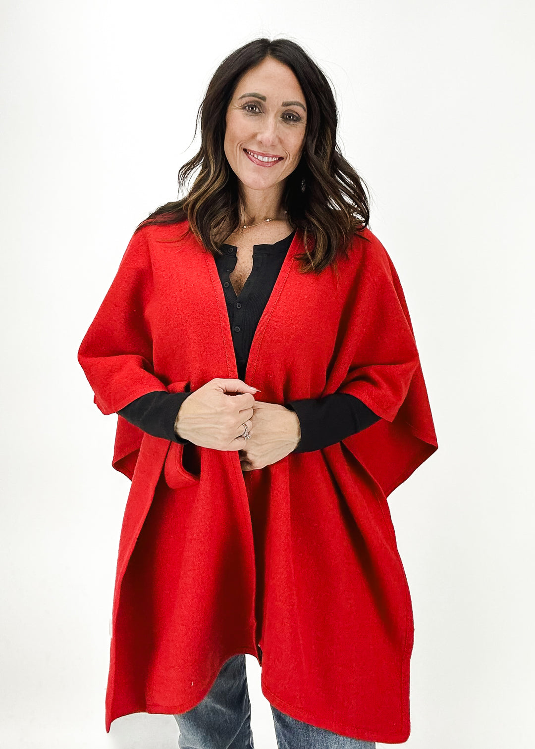 Dolce Cabo red knit wrap-front cardigan featuring a cozy design with an open front, perfect for layering on cool days. Model wearing the cardigan over a black top with light wash jeans.