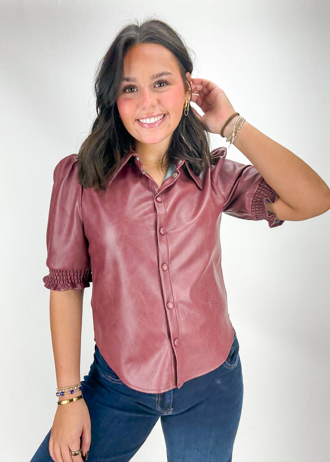 Woman wearing a pink leather blouse and blue jeans on a white background