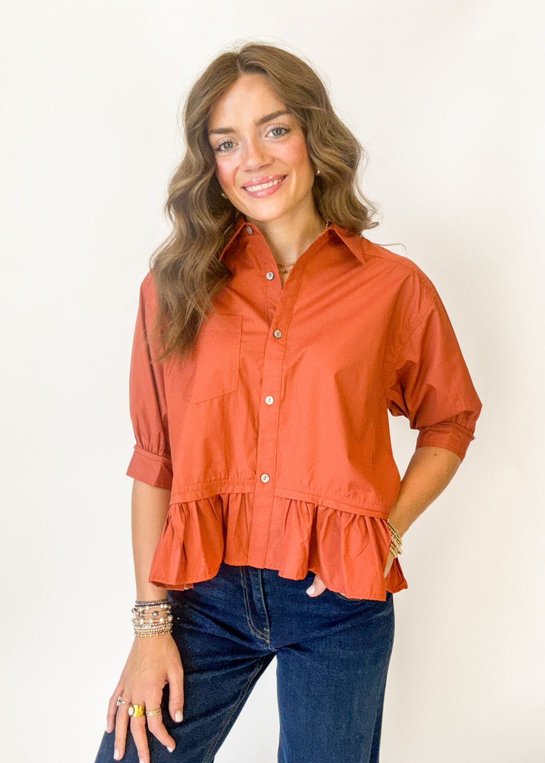 A woman wearing a rust colored top with button details and a ruffle at the bottom