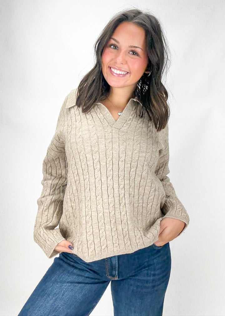 Woman wearing a beige cable knit sweater and blue jeans on a white background