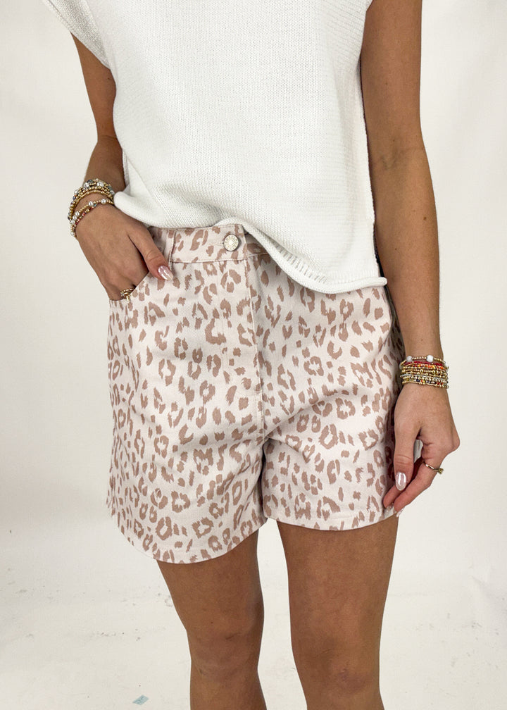Person wearing leopard print shorts and a white top on a plain background