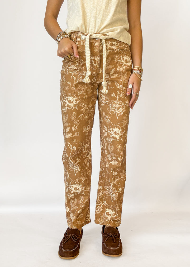 A person wearing tan pants with a cream floral print and a cream drawstring waist