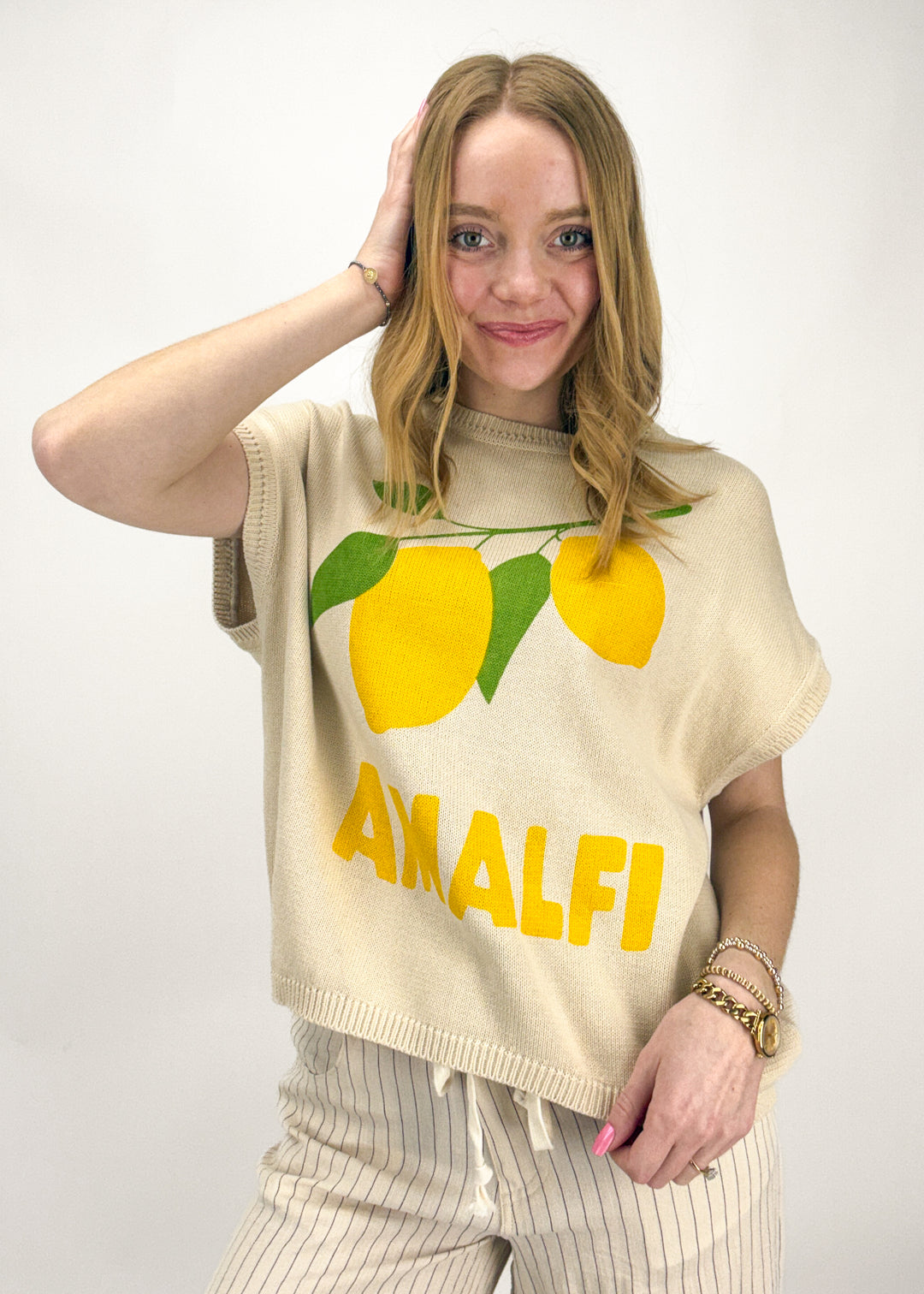 Woman wearing a beige sleeveless sweater with lemon graphics and 'Amalfi' text on a white background