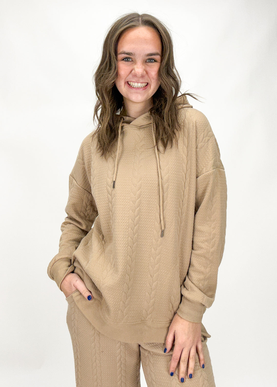 Woman wearing a beige cable knit hoodie and pants on a white background
