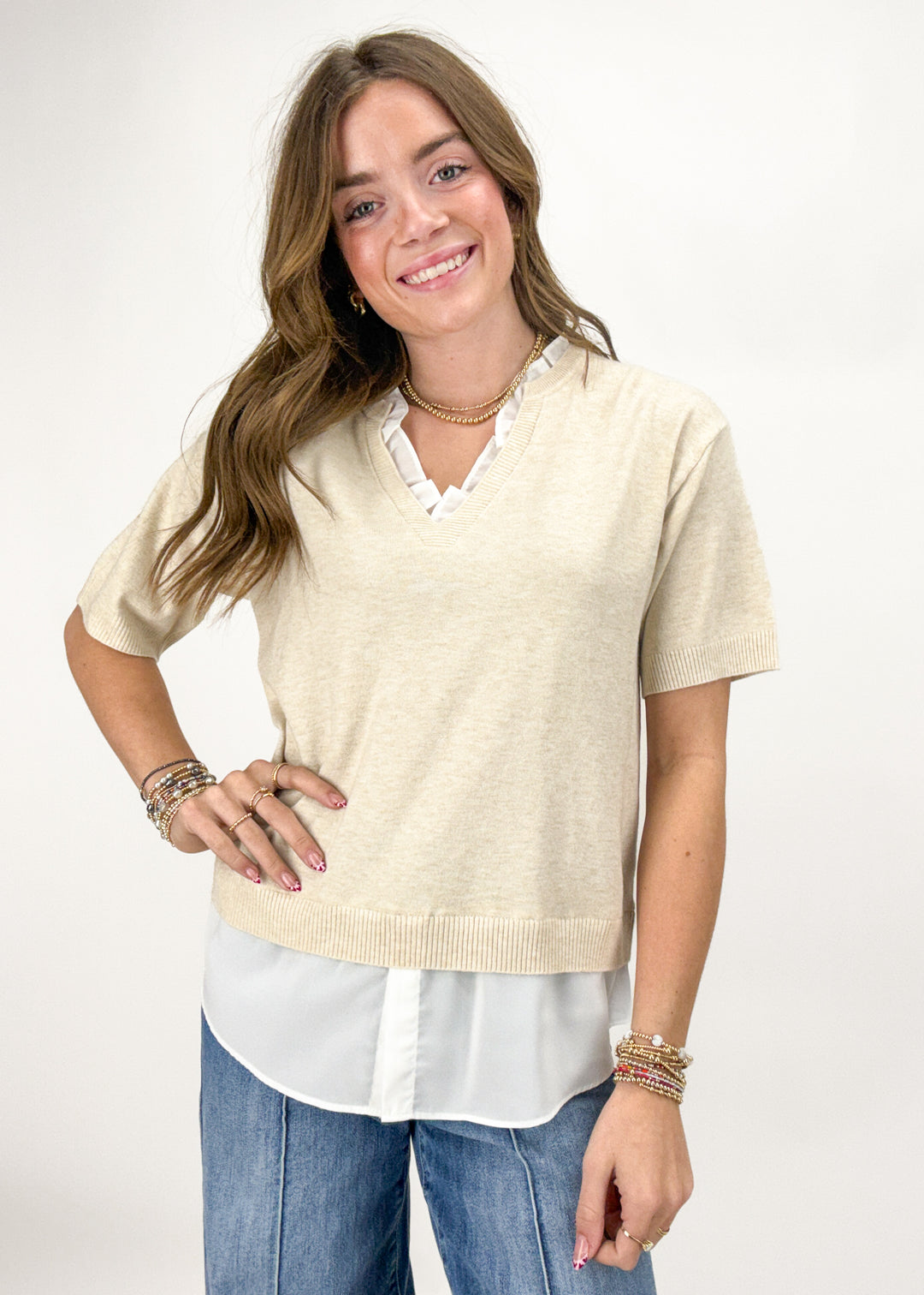 Woman wearing a beige sweater over a white shirt with blue jeans on a white background