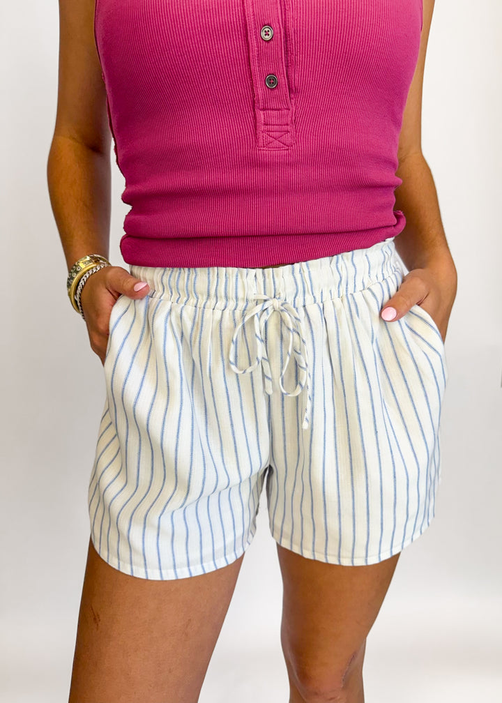 Person wearing a pink shirt and striped shorts on a white background