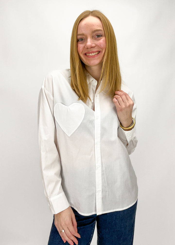 Woman wearing a white shirt with a heart design on a plain background