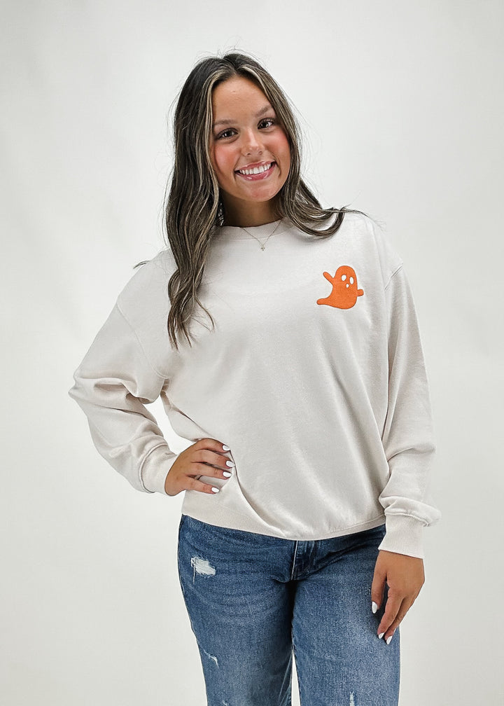 woman wearing white crew neck sweatshirt with orange puffy ghost on left chest