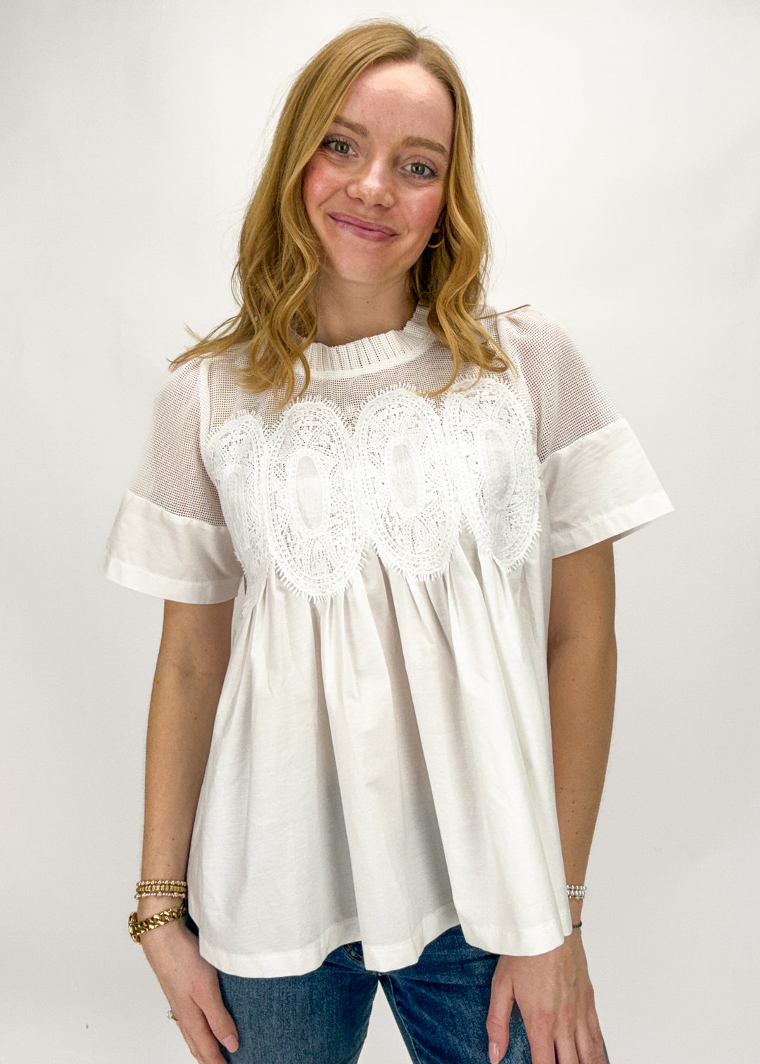 Woman wearing a white blouse with lace details on a plain background