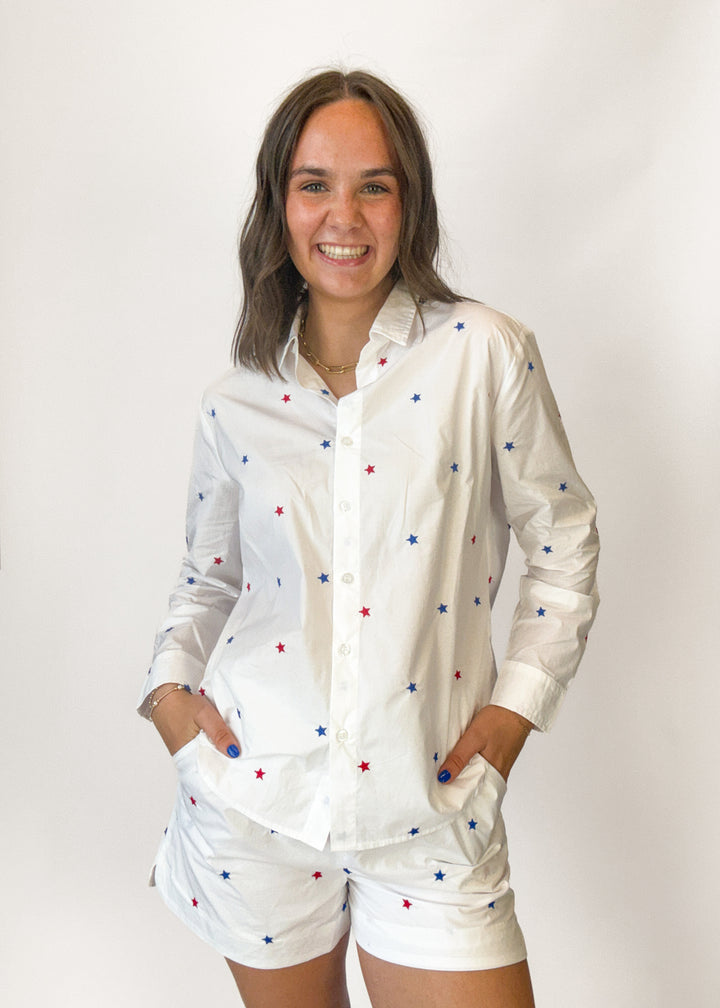 Woman wearing a white shirt with colorful star patterns and matching shorts on a plain background