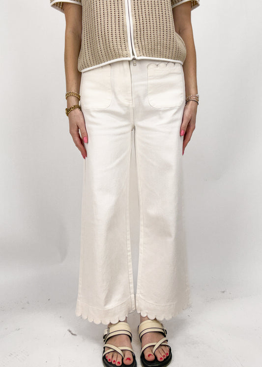 Person wearing a beige top and white pants on a white background