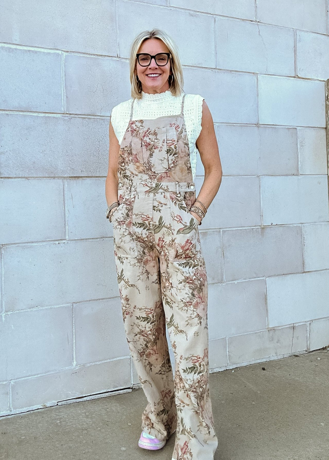 A woman wearing wide-leg floral print overalls with front pockets, styled with a textured sleeveless top for a casual and trendy look.