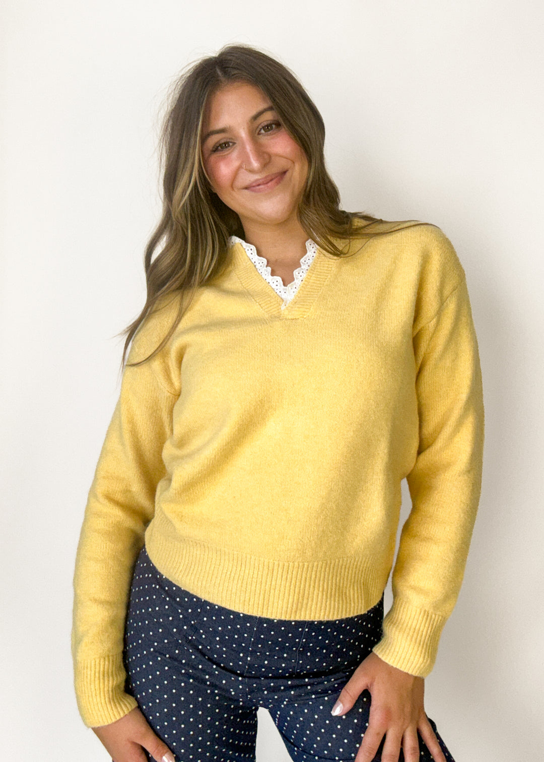 A woman wearing a pale yellow knit sweater with a white lace-trimmed V-neck collar, 